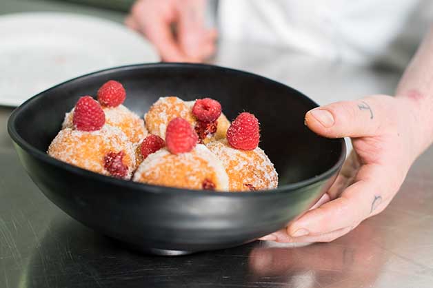 The chef has plated the donuts with fresh raspberries