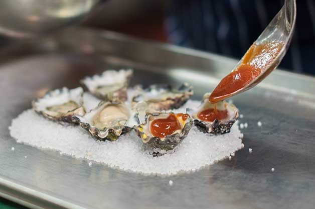 The chef adds a spoon of sauce to each oyster 