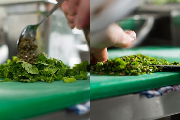 The chef is pictures slicing the fresh herbs and capers