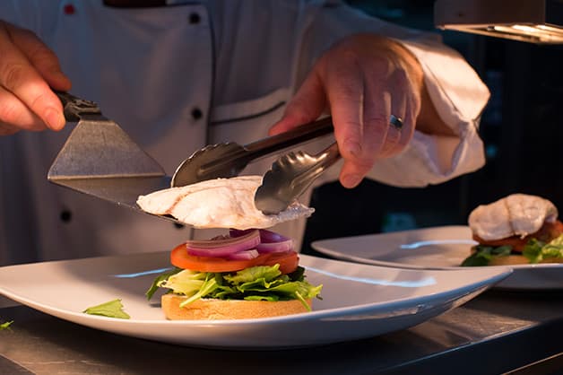 The chef is seen adding the barramundi to the burger