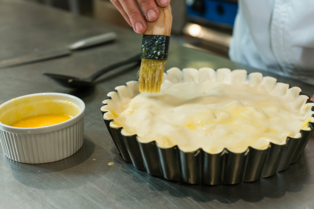 The chef brushes the lid of the pie with the egg wash