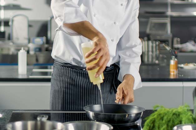 The photo shows a chef pouring oil into a hot pan